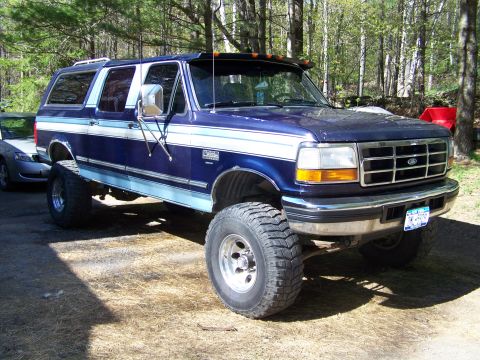 1979 Ford Bronco - A lifted two-tone blue and silver Ford crew cab pickup with a matching camper shell, shown from the front three-quarter angle on oversized…