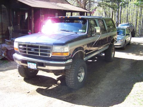 1979 Ford Bronco - A black lifted Ford full-size Bronco parked on a dirt driveway, shown from the front three-quarter angle with chrome grille, Ford badge, ov…