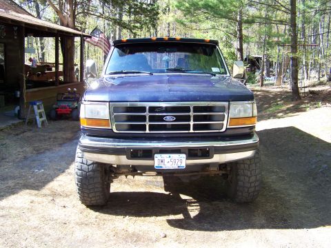1979 Ford Bronco - Front view of a dark blue Ford pickup truck with a lift kit and large off-road tires, chrome grille with Ford oval, and a New York license…