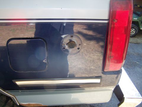 1979 Ford Bronco - Close-up of the rear body panel of a dark blue and white two-tone vehicle, showing a square fuel-door recess and a round metal mounting fla…