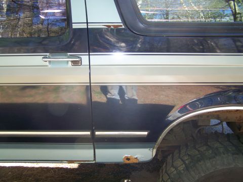 1979 Ford Bronco - Close-up side view of a dark blue two-tone SUV showing the rear door, chrome door handle, body-side molding, and rear wheel arch with a mud…