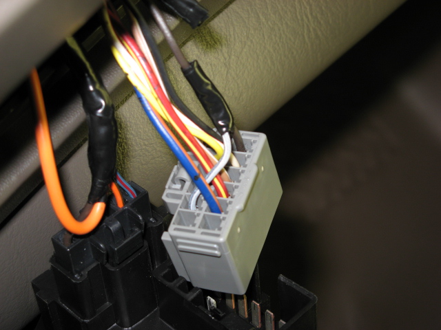 Gray wiring harness connector with spliced wires wrapped in electrical tape under a dash