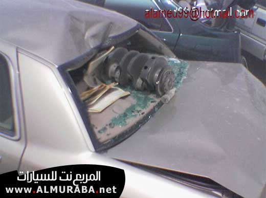 Car's rear window is smashed, and a crankshaft is visible inside. Another car is in the background