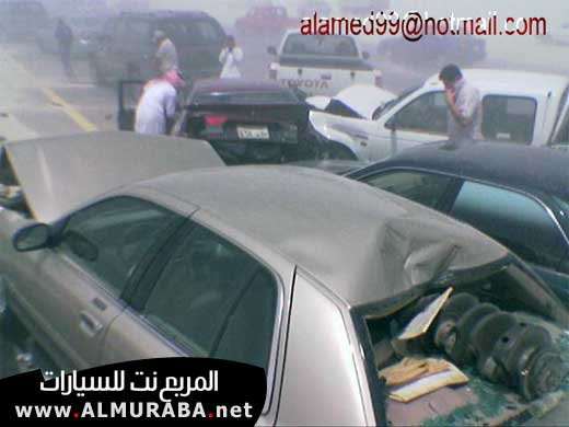 Silver sedan with a crushed roof, showing engine parts, next to other damaged vehicles on a highway