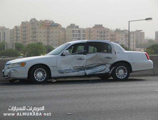 White sedan with heavy side damage, parked on the side of a road