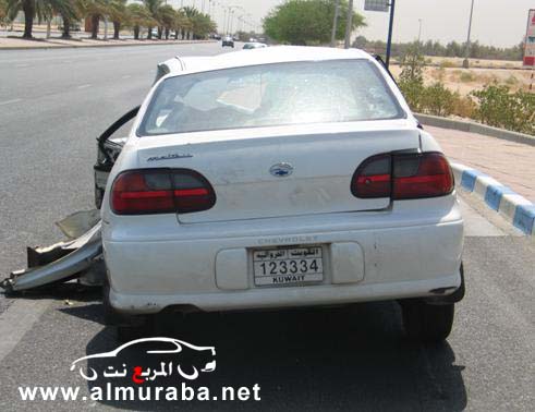 White sedan with rear-end damage, driver's door ajar, and bent bumper