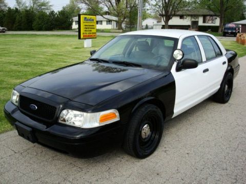 2003 Ford Crown Victoria - Two-tone police car, black front and white rear, parked outdoors on a paved surface.