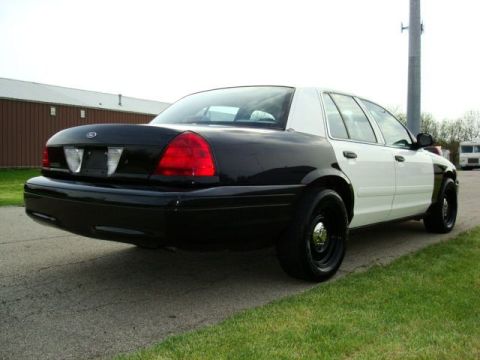 2003 Ford Crown Victoria - This black and white police car, likely a 2003 Ford Crown Victoria, is shown from the rear three-quarter angle.