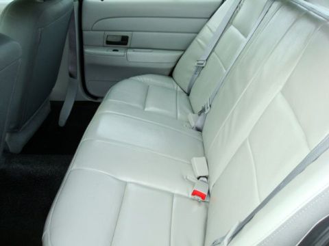 2003 Ford Crown Victoria - The rear interior of a vehicle shows light-colored leather seats with seatbelts and a portion of the door panel.