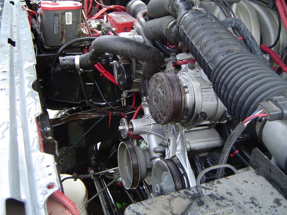 Engine bay close-up showing serpentine accessory drive, A/C compressor and red plug wires
