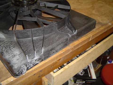 1989 Ford Bronco - A damaged electric fan shroud shows signs of repair with adhesive, resting on a workbench with boxes in the background.