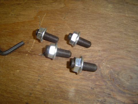 1989 Ford Bronco - Four bolts with integrated washers and nuts, along with an Allen wrench, are laid out on a wooden surface.