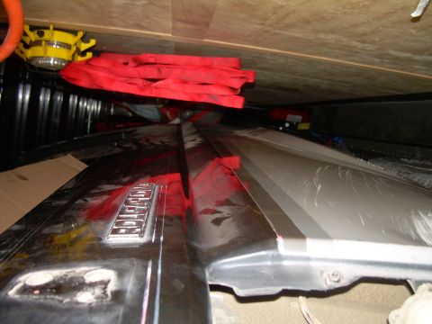 1986 Ford Bronco - A close-up view of a 'BRONCO' emblem on a vehicle's fender, with red straps and a yellow light visible overhead.
