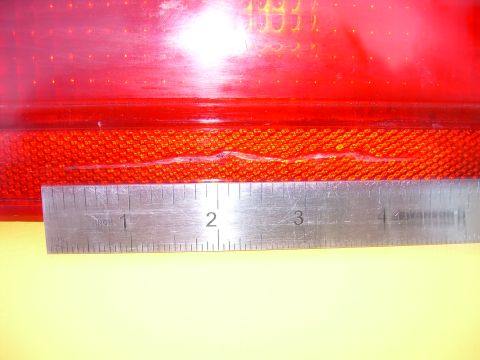 1986 Ford Bronco - A ruler is placed against a damaged red taillight lens, showing the extent of the crack.