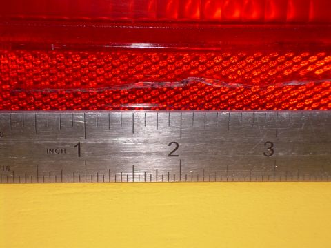 1986 Ford Bronco - A ruler measures the damage on a red vehicle tail light lens.
