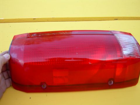 1986 Ford Bronco - Red taillight assembly for a vehicle, held by a hand against a yellow background.