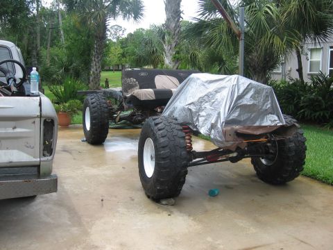 1974 Ford F-100 - A disassembled truck chassis sits on a concrete driveway next to another truck, with one section covered by a tarp.
