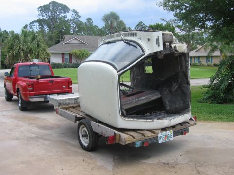 1974 Ford F-100 - A truck cab is transported on a trailer, pulled by a red pickup truck.