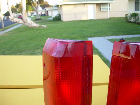 1986 Ford Bronco - Close-up of two red tail lights, likely for a vehicle, against a blurred suburban backdrop.