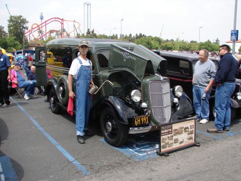 1992 Ford Taurus - A person in overalls stands next to a vintage green Ford panel truck at a car show.