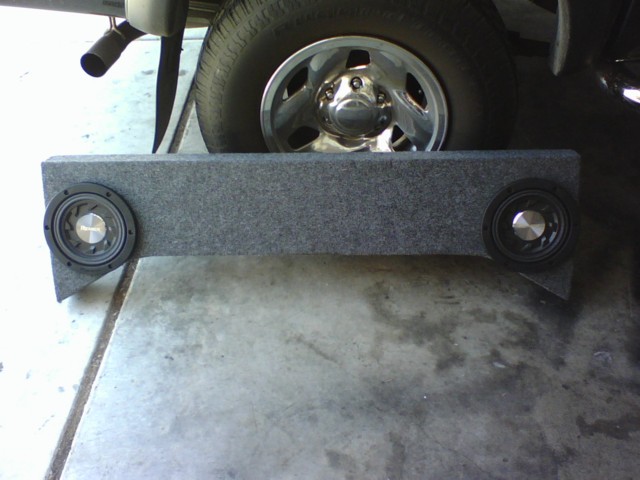 Car stereo subwoofer box with two Pioneer speakers, placed in front of a vehicle tire and exhaust pipe
