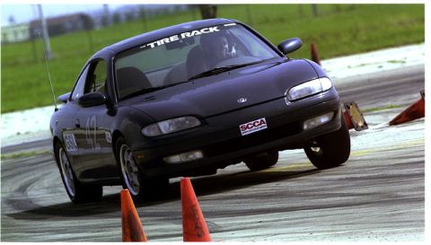1991 Ford Probe - A black Mazda MX-6 navigates a race course, marked with "Tire Rack" on the windshield and an SCCA sticker.