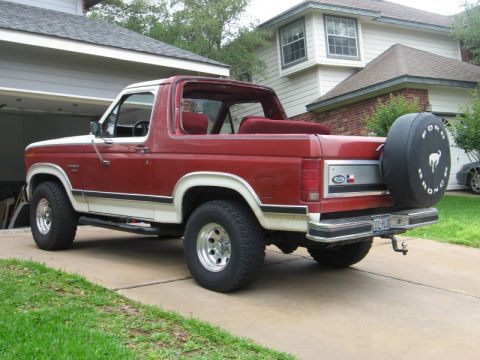 1986 Ford Bronco - This red and white 1986 Ford Bronco features a removable top and a spare tire cover with the Bronco logo.