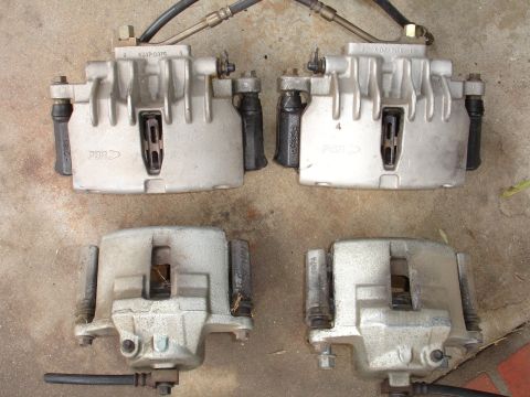 1993 Ford Taurus - Four brake calipers are shown, two larger ones above two smaller ones, on a concrete ground.