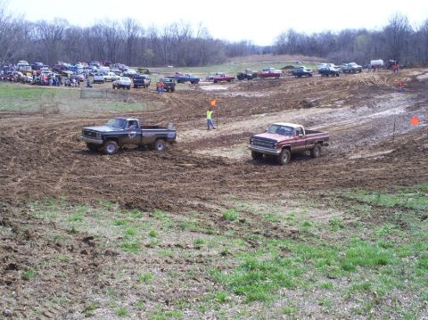 2001 Dodge 1500 - Pickup trucks navigate a muddy track during a race event, with spectators gathered in the background.
