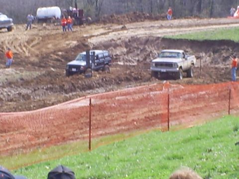 2001 Dodge 1500 - Trucks navigate a muddy course during an event, with spectators and equipment visible in the background.