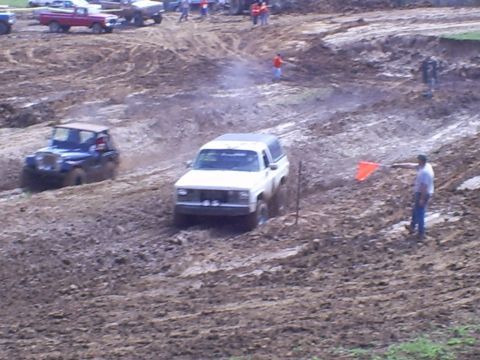 2001 Dodge 1500 - A white SUV navigates a muddy track during an off-road event, with a flagger signaling.