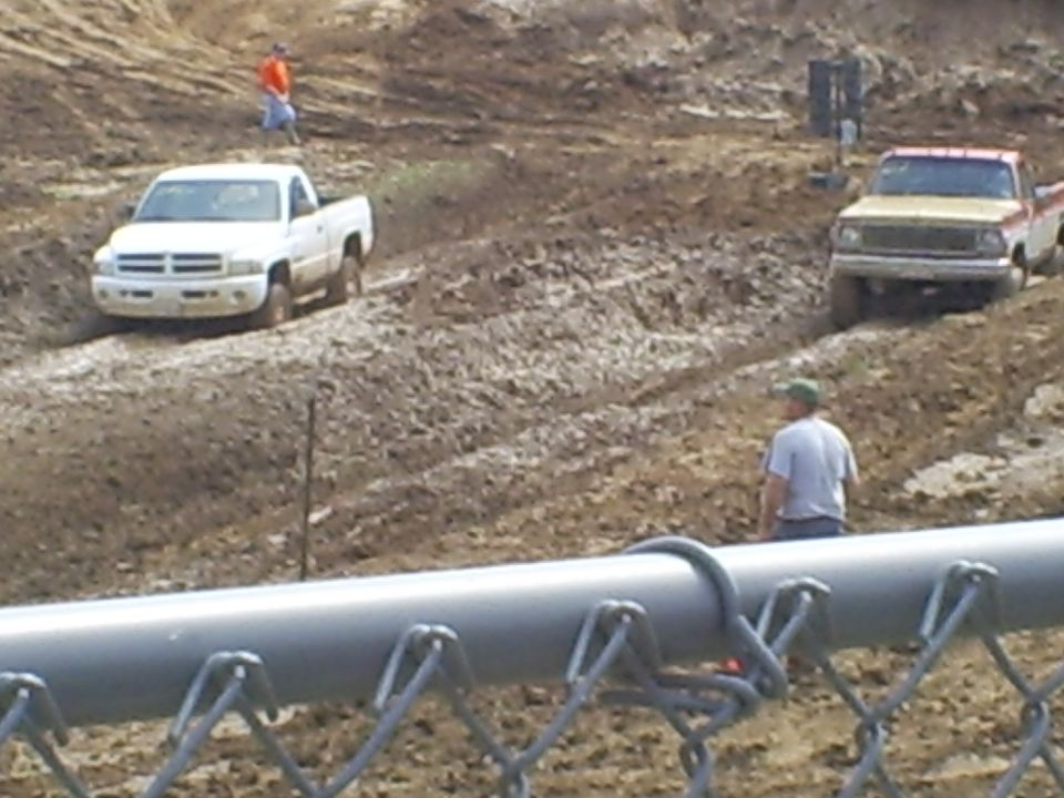 White Dodge Ram pickup and older two-tone truck in a muddy off-road pit