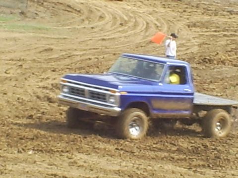 2001 Dodge 1500 - A blue Ford pickup truck navigates a muddy track during a race event.