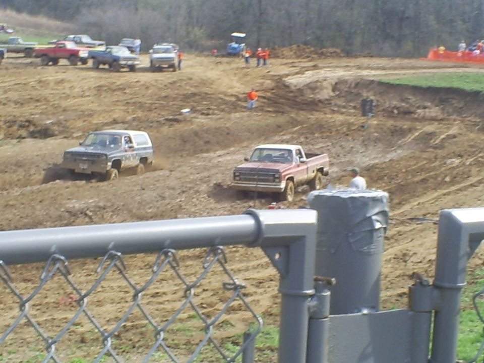 Square-body Chevy Blazer and pickup running a muddy mud-bog pit