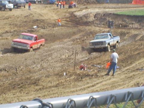 2001 Dodge 1500 - Two pickup trucks compete in a mud race, with spectators watching from the sidelines.