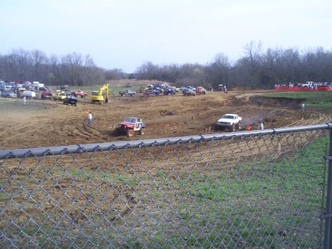 2001 Dodge 1500 - Off-road vehicles compete in a mud bogging event on a dirt track with spectators in the background.