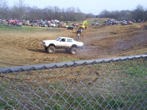 2001 Dodge 1500 - A modified sedan navigates a muddy track during an event, with numerous vehicles and people gathered around.