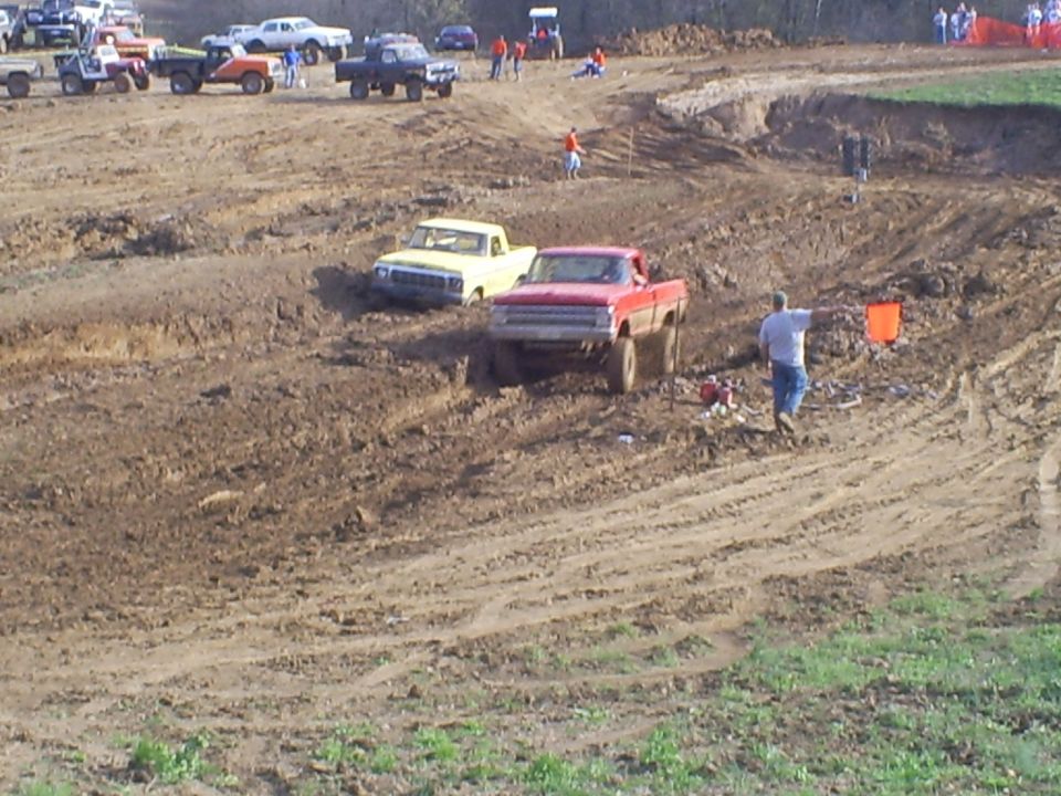 Muddy track with several trucks, one red and one yellow, navigating the terrain