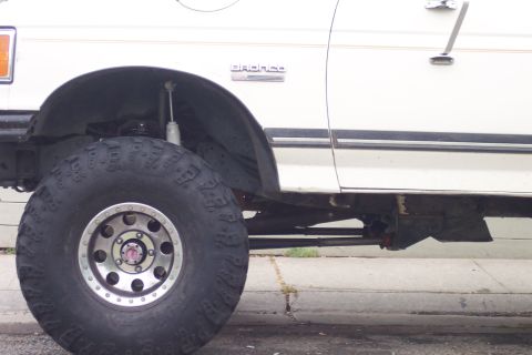 1989 Ford Bronco - A 1989 Ford Bronco is shown from the side, highlighting its large off-road tire and suspension modifications.