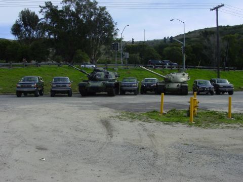 1994 Ford Bronco - Several SUVs are parked in front of two military tanks on a cloudy day.