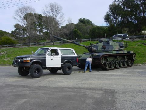 1994 Ford Bronco - A Ford Bronco tows a military tank, with a person attending to the tow hitch.