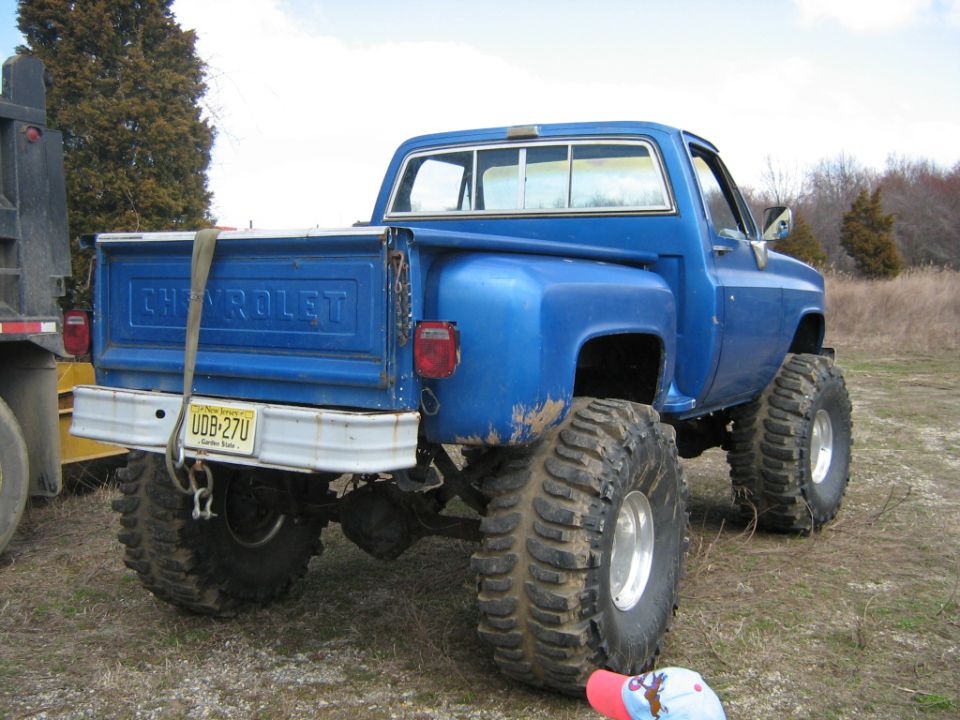 Blue Chevrolet pickup truck with oversized tires and lifted suspension, rear view