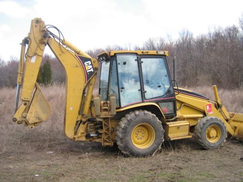 1990 Ford Bronco - A yellow Caterpillar backhoe loader sits in a field, its loader arm extended.