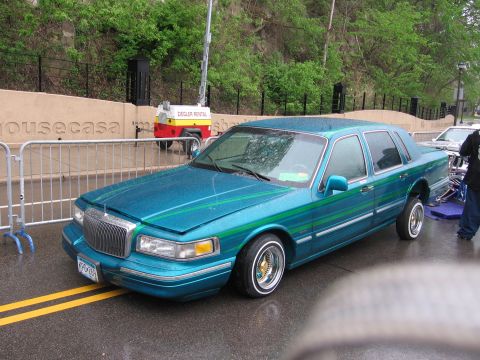 1998 GMC Sierra 1500 - A customized sedan with a unique paint job and lowered suspension is parked on a wet street.