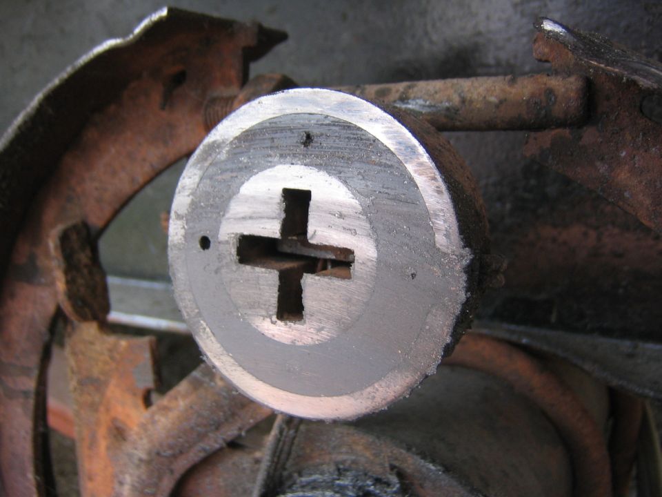 Close-up of a rusty brake drum with a large cross-shaped slot in the center