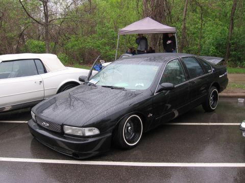 1998 GMC Sierra 1500 - A black sedan with custom wheels is parked on a wet asphalt surface next to a white convertible.