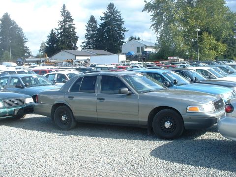 2000 Ford Crown Victoria - A row of vehicles are parked on a gravel lot under a cloudy sky.