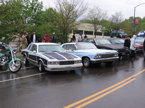 1998 GMC Sierra 1500 - A line of classic cars, including a distinctive 1980s Chevrolet Monte Carlo, are parked outdoors on a rainy day.