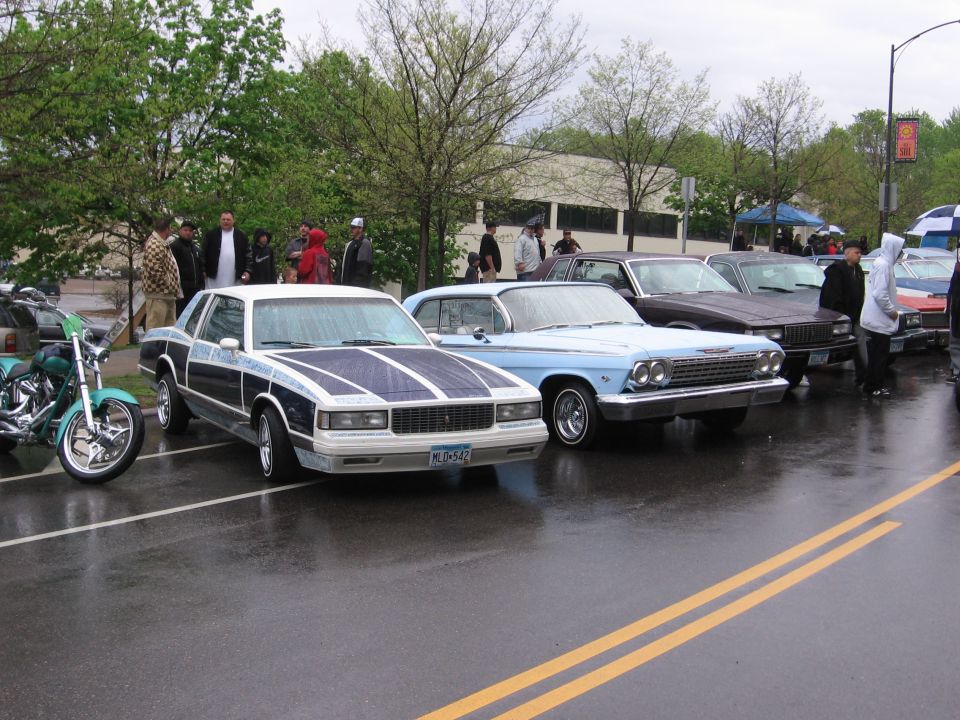 Blue and white 1980s Chevrolet Monte Carlo with custom stripes, parked on wet asphalt
