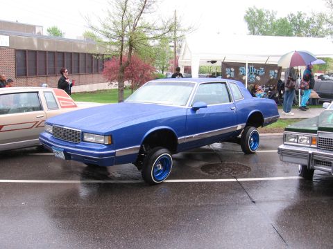 1998 GMC Sierra 1500 - A blue lowrider car is parked on a wet street next to other vehicles.
